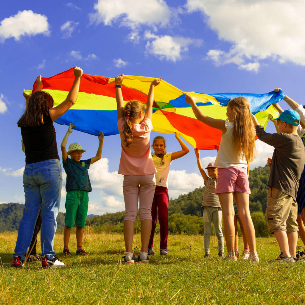 Children playing with a rainbow-colored parachute